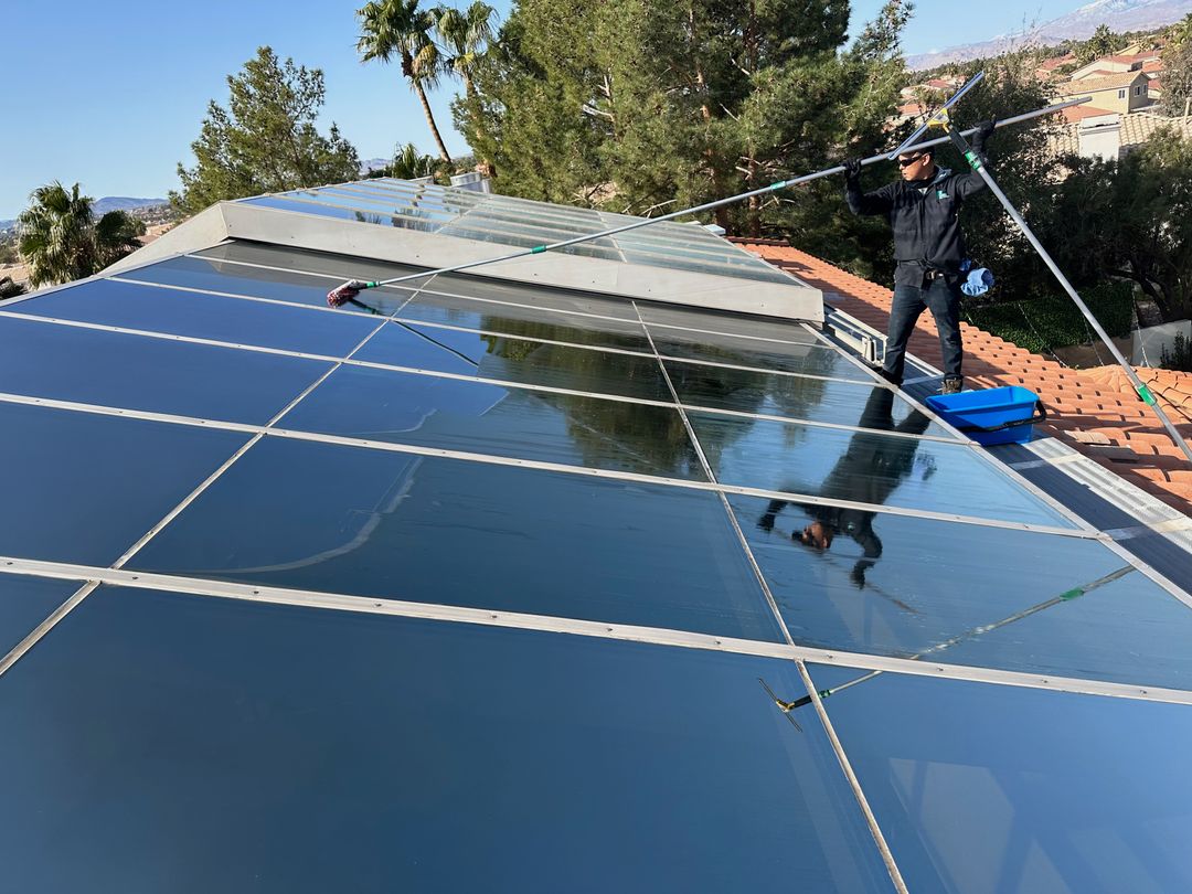 A man uses a long wiper to clean the glass roof of a house, ensuring it is free from dirt and debris