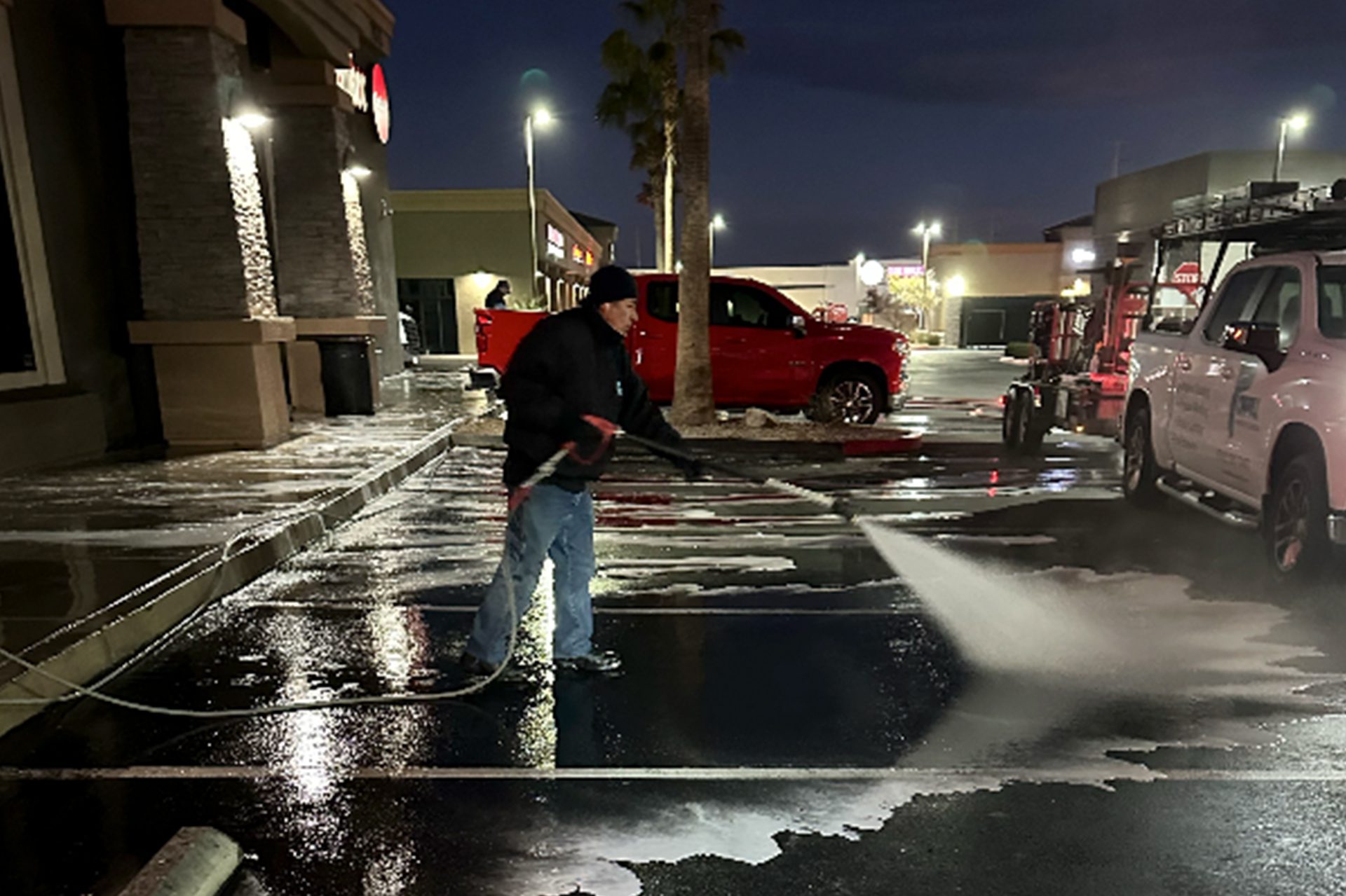 A man is engaged in washing a parking  lot under the night sky, with ambient light highlighting his careful work and dedication